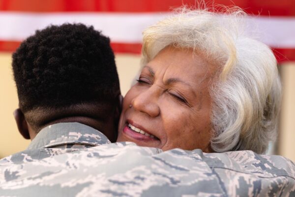 Contented senior african american woman hugging military son outside house. family, bonding and patriotism, unaltered