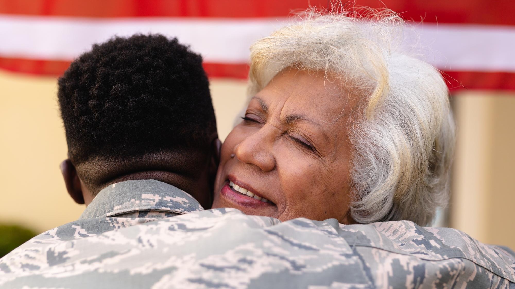Contented senior african american woman hugging military son outside house. family, bonding and patriotism, unaltered