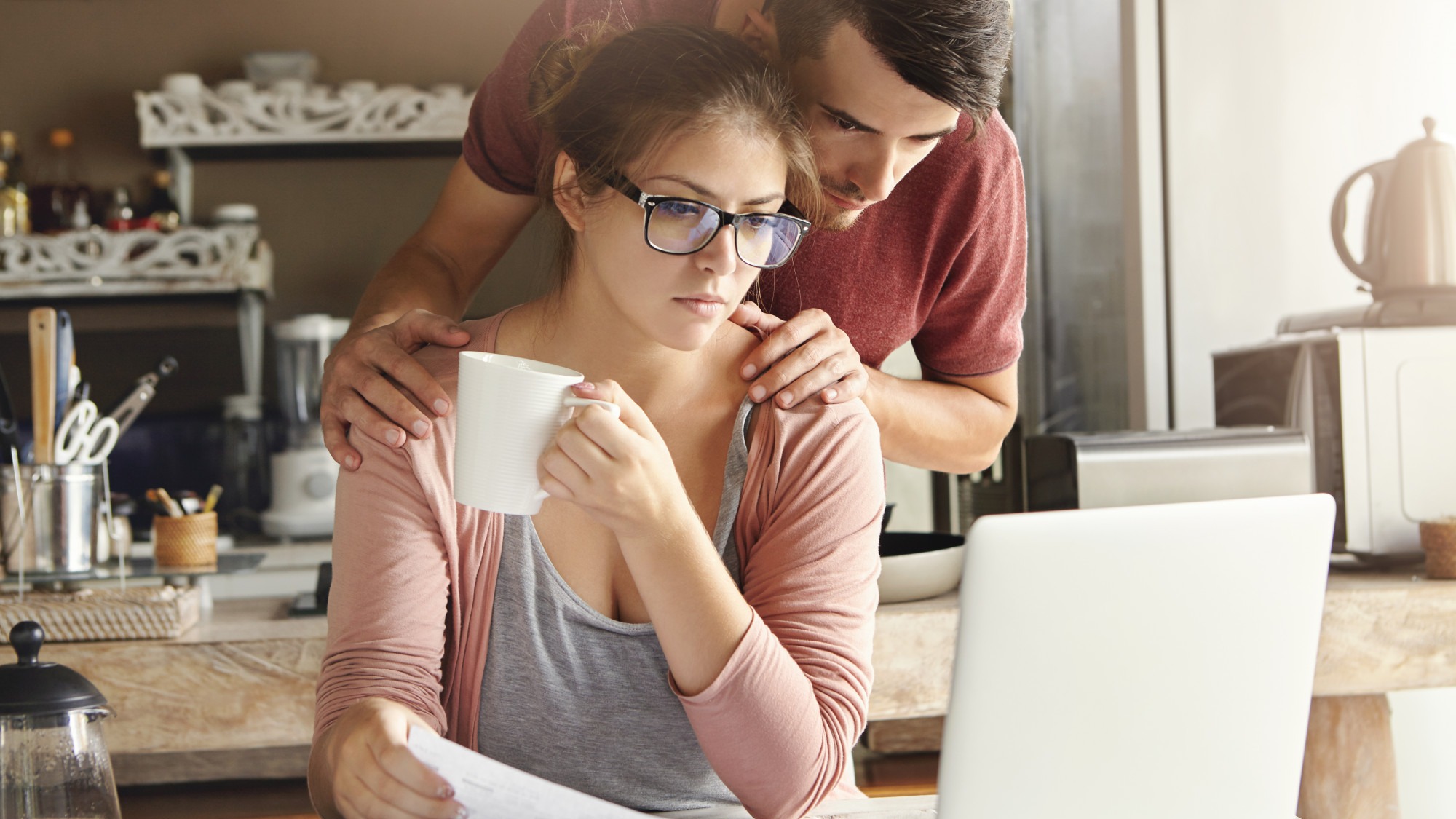 Frustrated young husband and wife doing paperwork together, calculating their expenses, managing bills, using laptop computer and calculator in modern kitchen