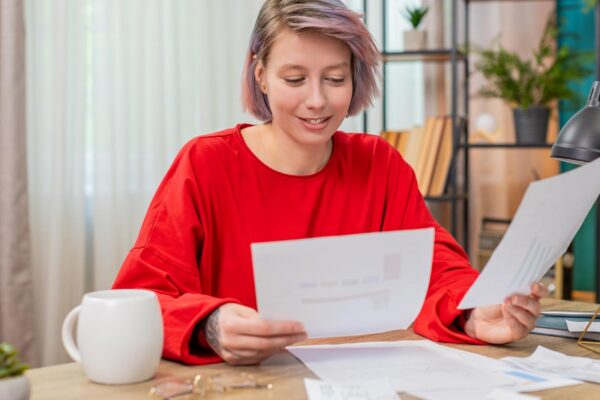 Young woman happily reviewing financial documents nodding positively satisfied successful results