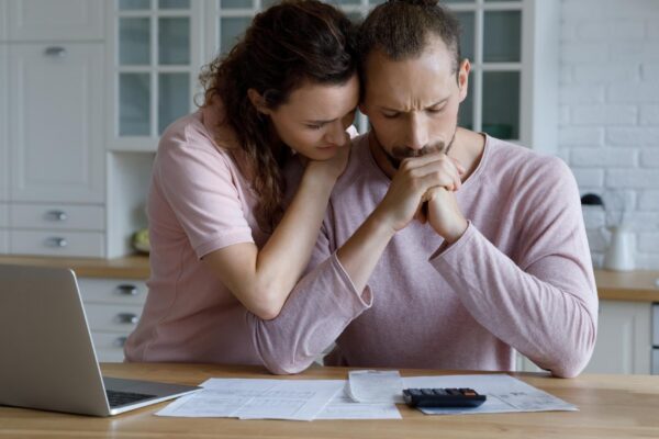 Unhappy young woman supporting stressed husband feeling depressed having financial problems calculating bills planning budget together at home suffering from lack of money bankruptcy concept