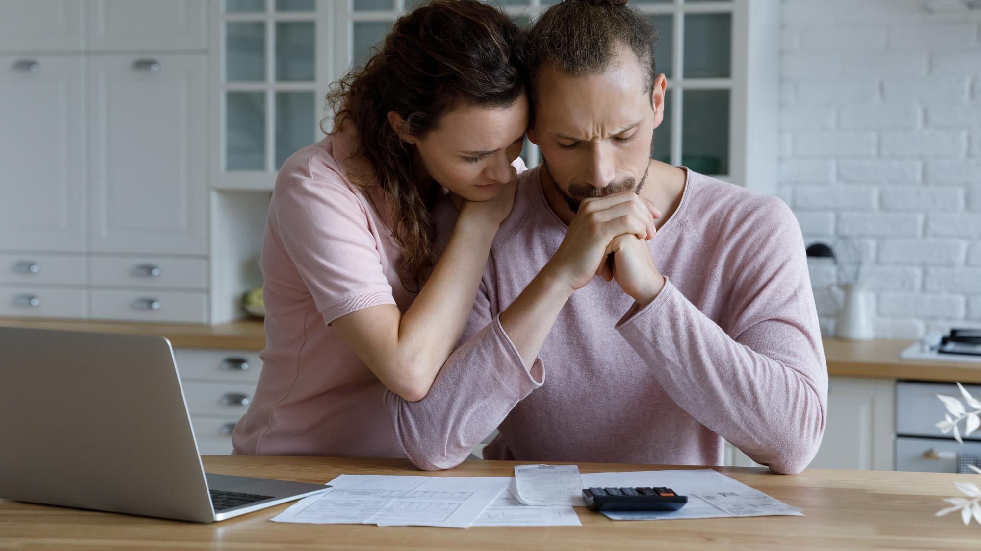 Unhappy young woman supporting stressed husband feeling depressed having financial problems calculating bills planning budget together at home suffering from lack of money bankruptcy concept