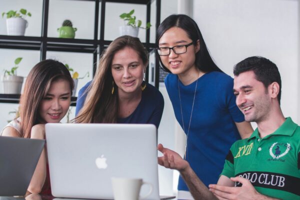 four people watching on white MacBook on top of glass-top table