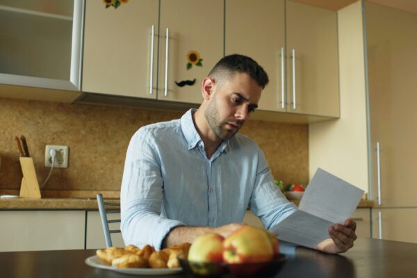 Man reading document at kitchen table with fruit and fruit