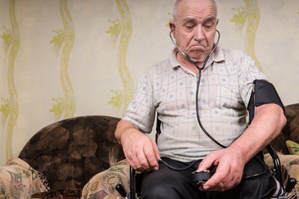 Thoughtful Old Bald Man with Blood Pressure Apparatus, Sitting on his Wheelchair In the Living Room with his Medicines on top of the Table.