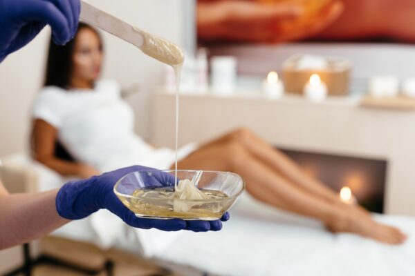 Beautician depilating young womans legs with liquid sugar in spa center. depilation of legs with turquoise shugaring paste.
