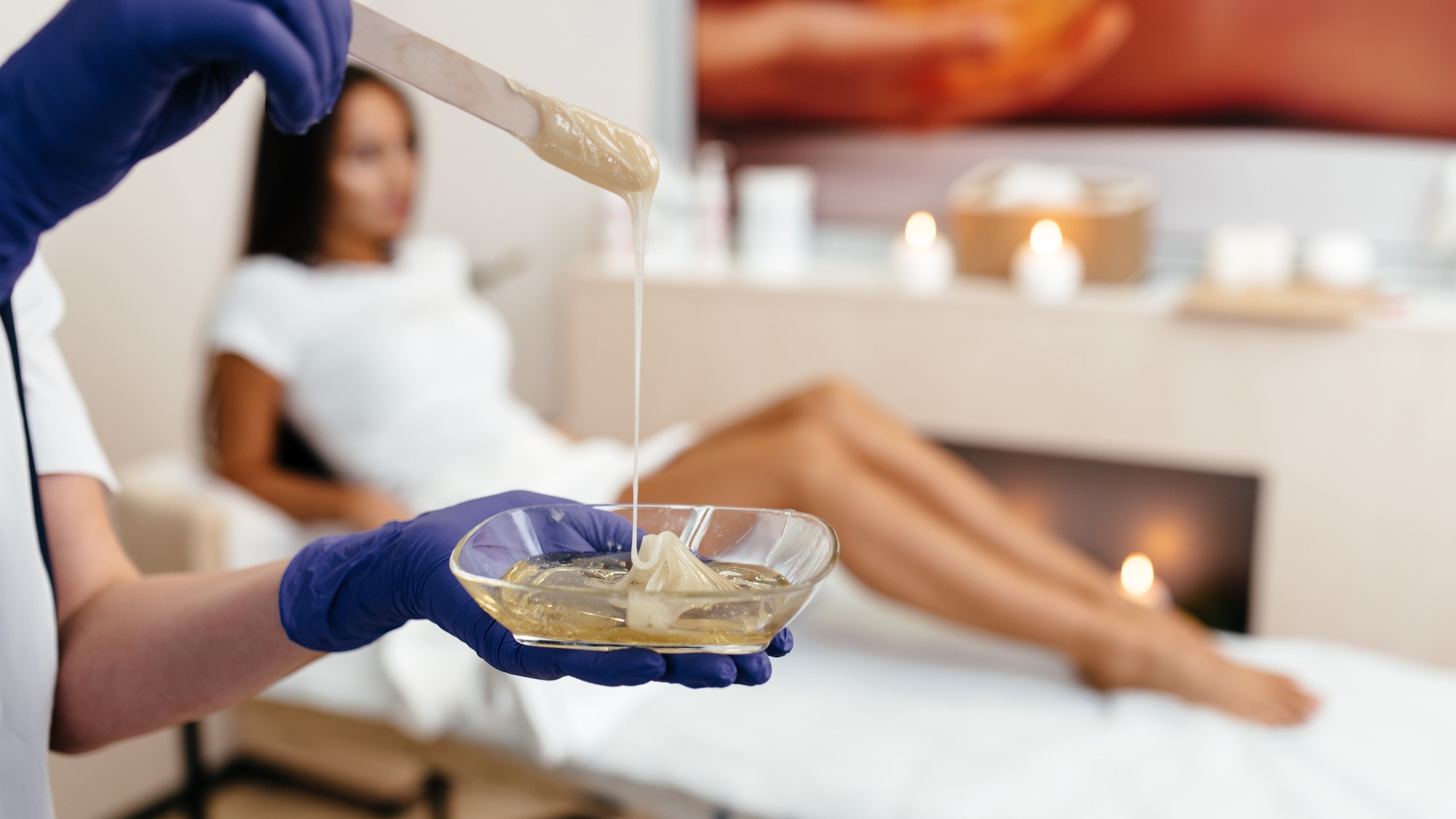 Beautician depilating young womans legs with liquid sugar in spa center. depilation of legs with turquoise shugaring paste.
