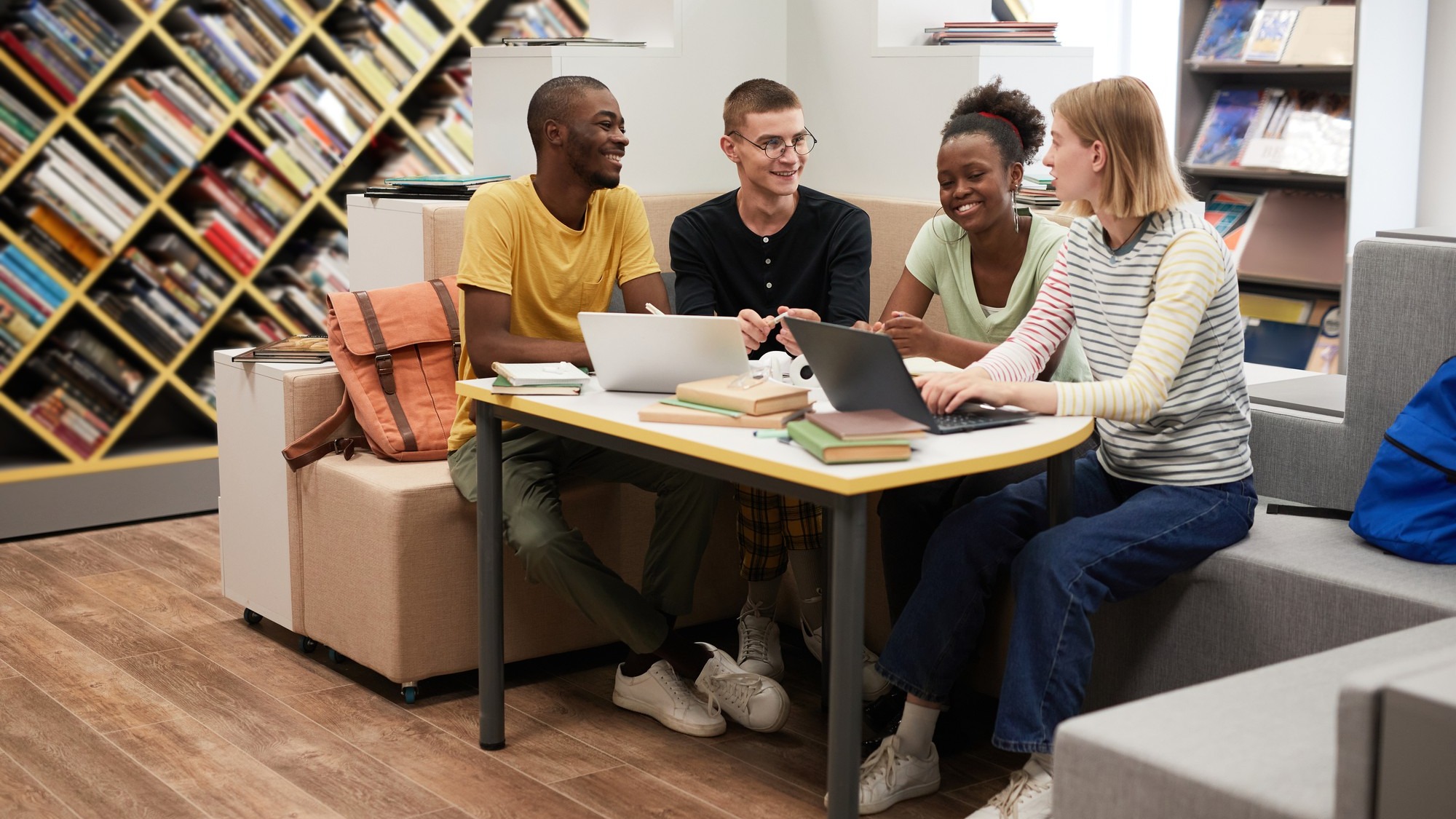 Full length view at diverse group of young people studying together at table in college library copy...
