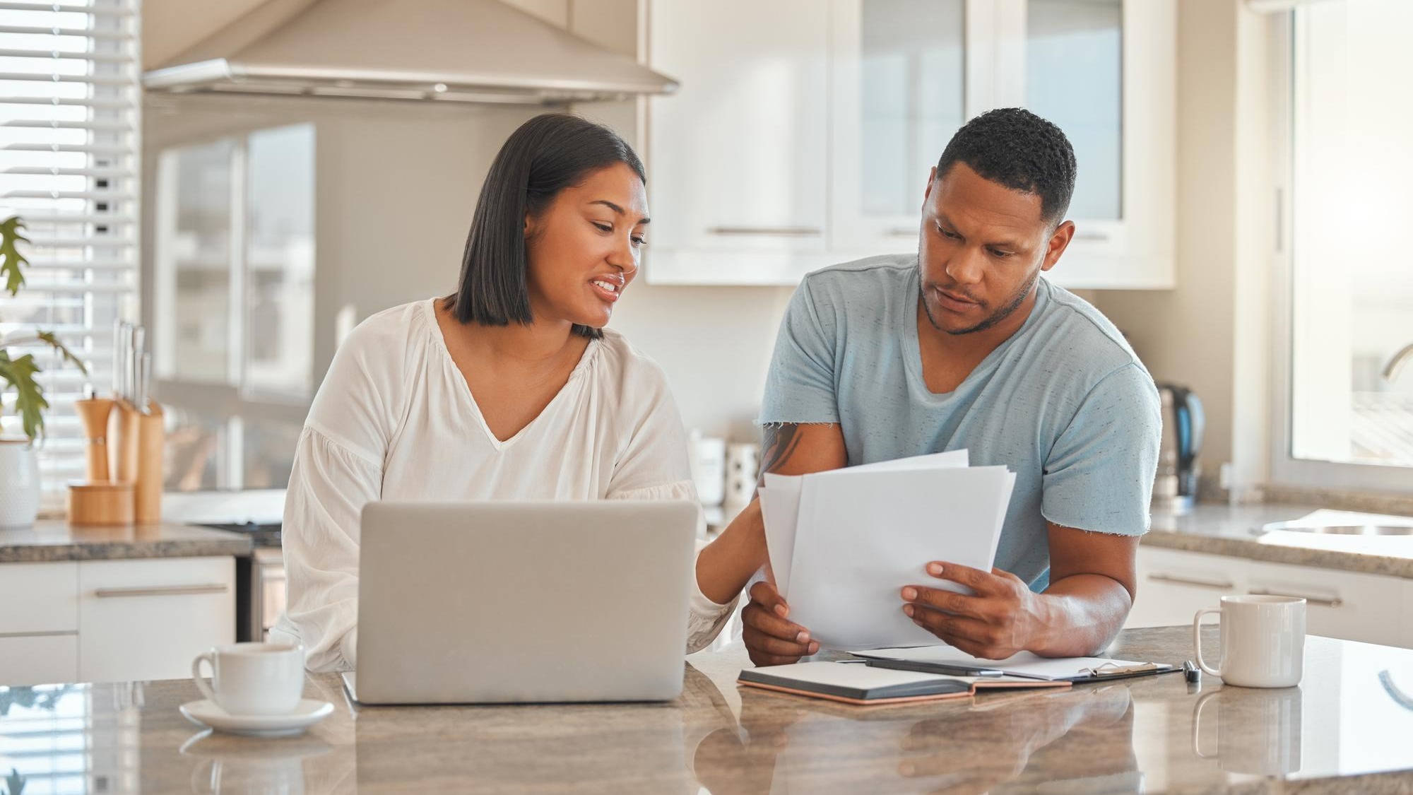 Couple laptop and paper in home for discussion online banking and travel budget Man woman or document in kitchen with tech invoice payment or explain contract for property investment opportunity