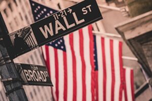 Wall street sign in New York with American flags and New York Stock Exchange in background