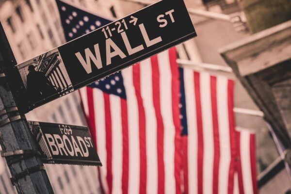 Wall street sign in New York with American flags and New York Stock Exchange in background