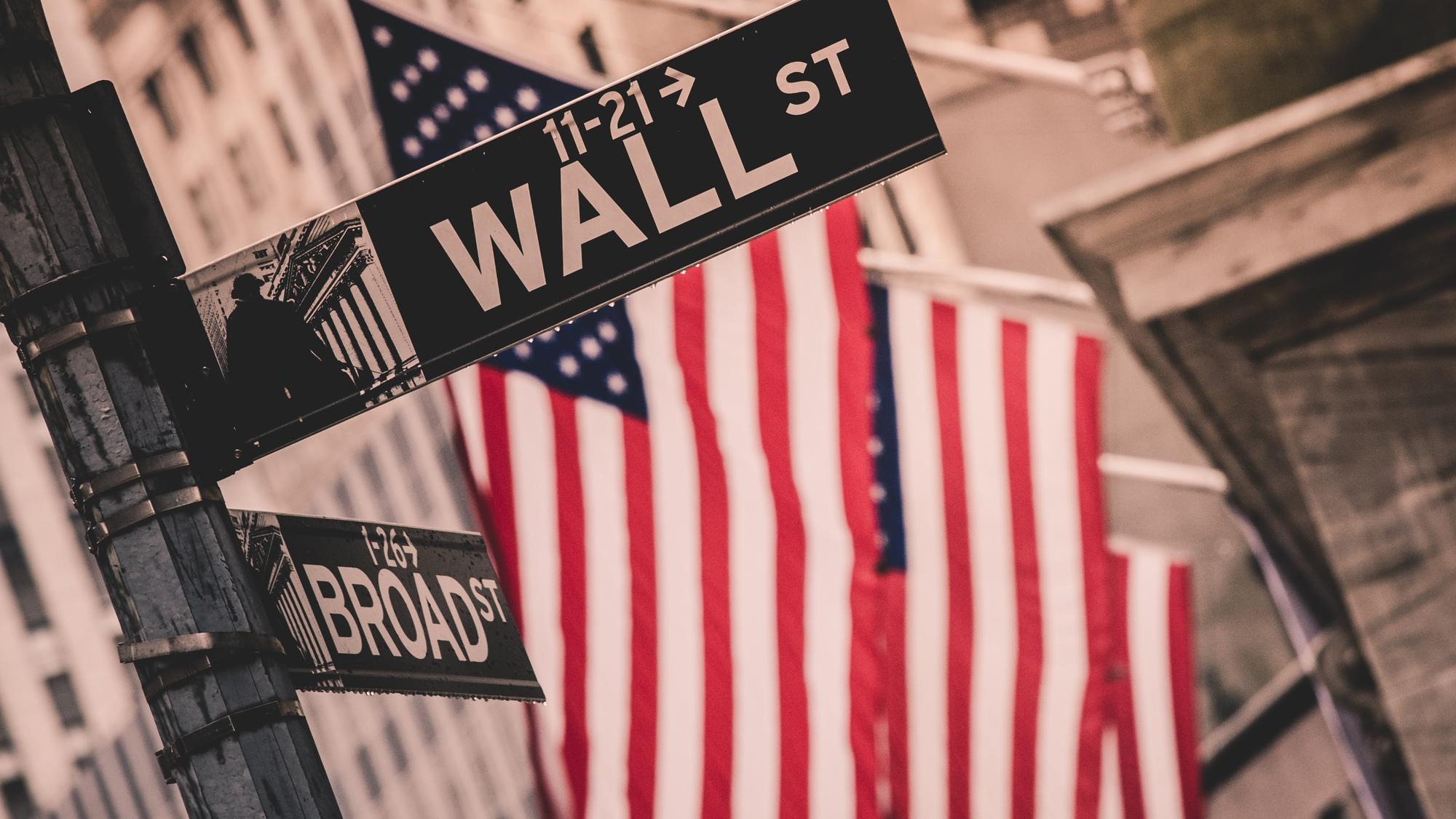 Wall street sign in New York with American flags and New York Stock Exchange in background