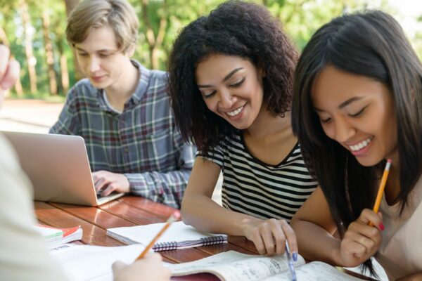 Happy students sitting and studying outdoors while talking.