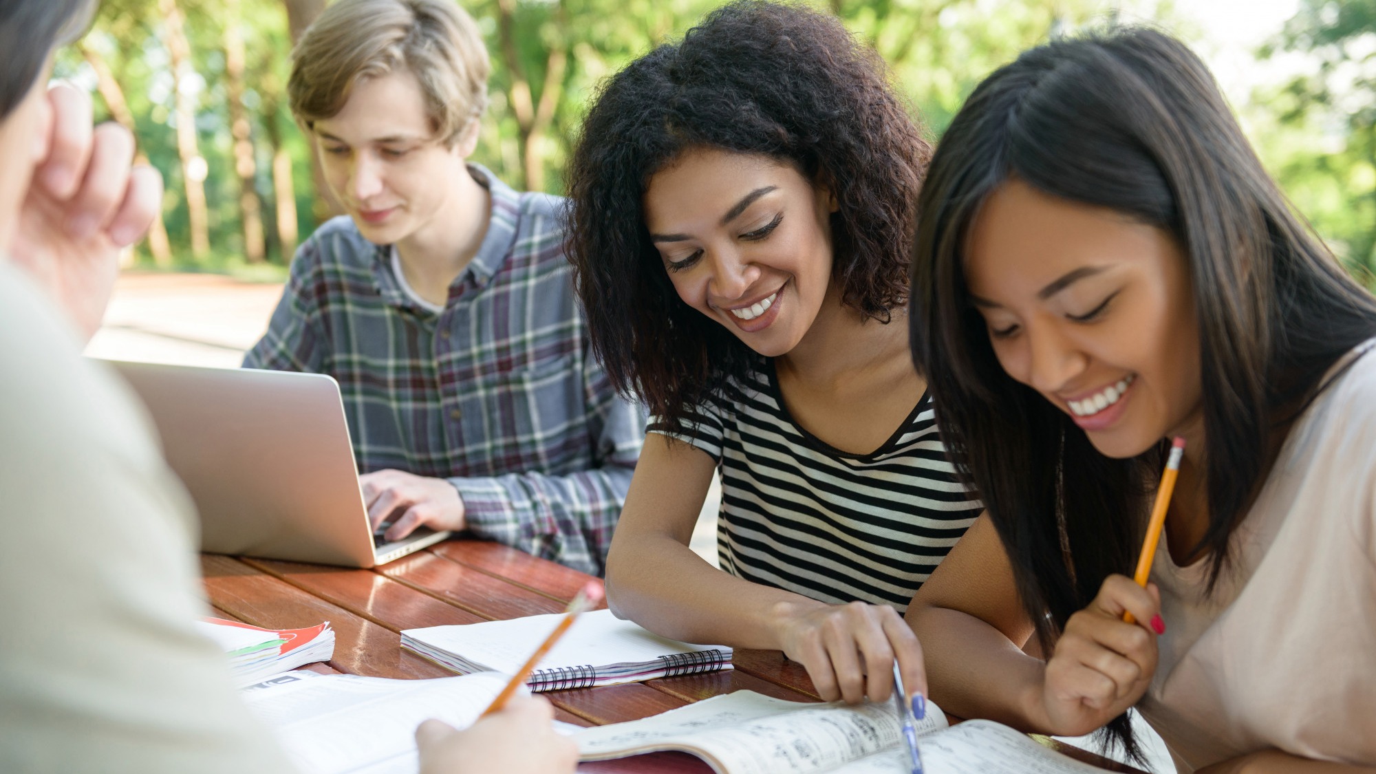 Happy students sitting and studying outdoors while talking.