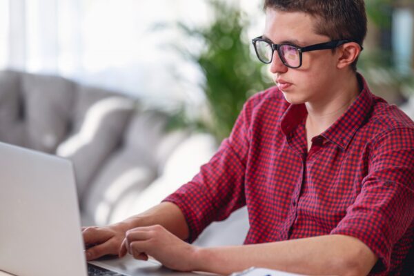 Brooding teen guy in glasses, listens to lecture, does in notebook, using laptop