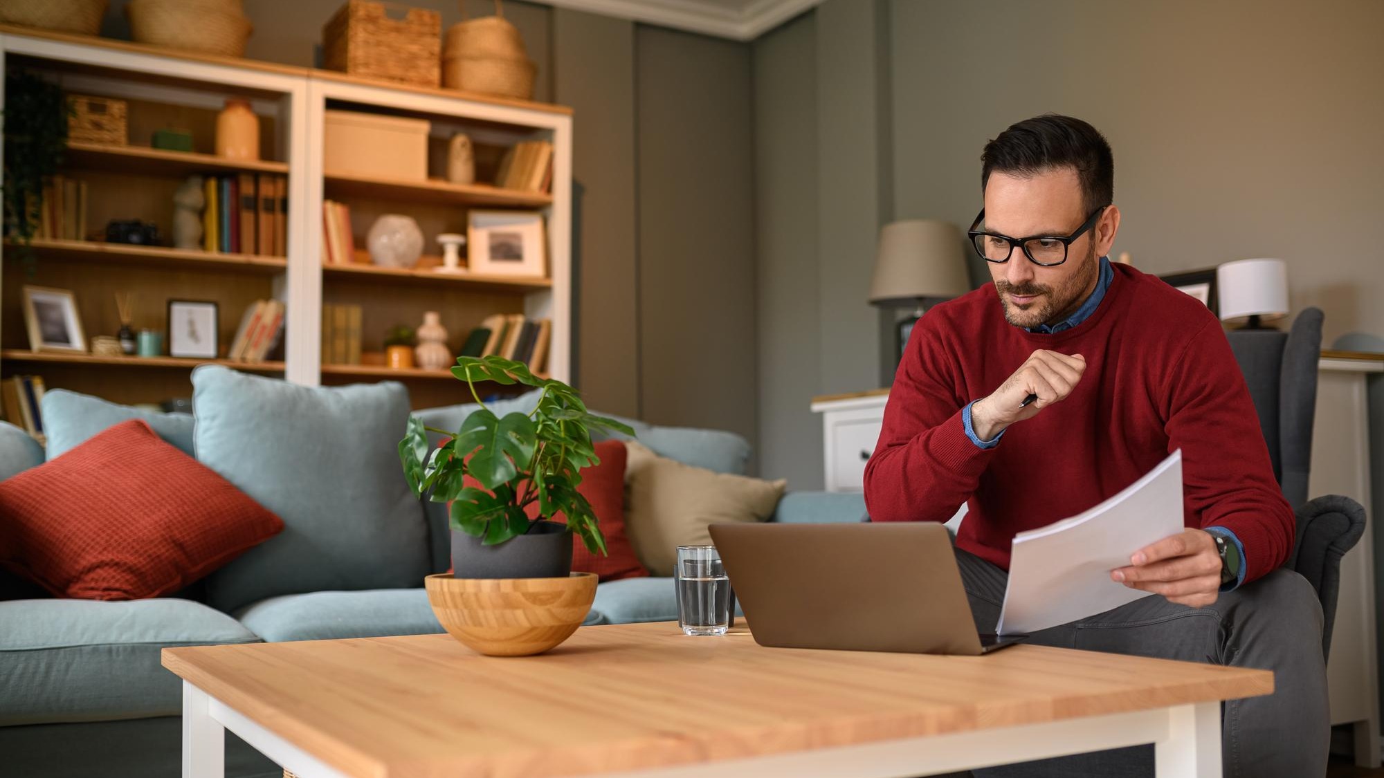 Focused businessman with documents reading information online over laptop on table at home office