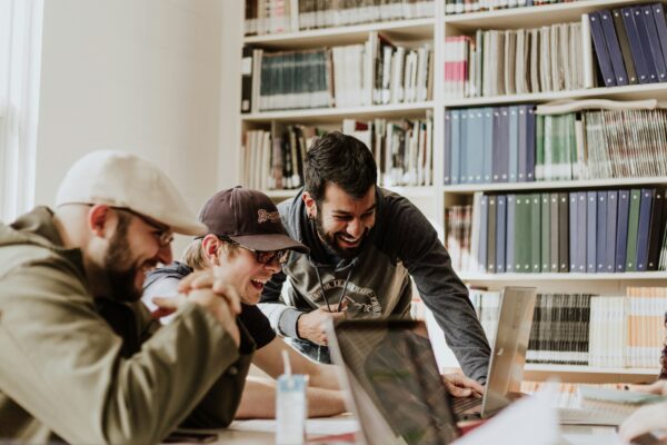 three men laughing while looking in the laptop inside room