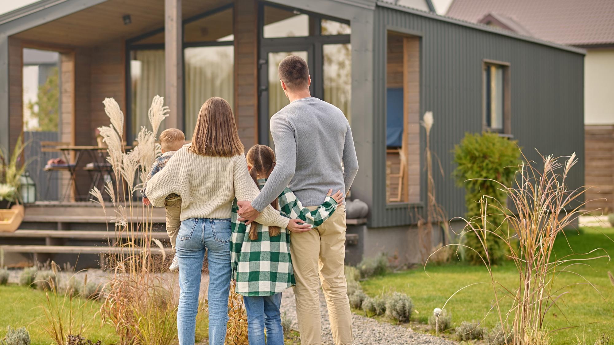 Back view of family hugging and admiring their home