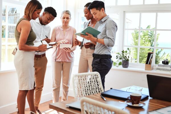 Business coach startup team workshop and mature business woman coaching men and women in modern office Diversity teamwork and writing note on strategy and planning advice from mentor or consultant