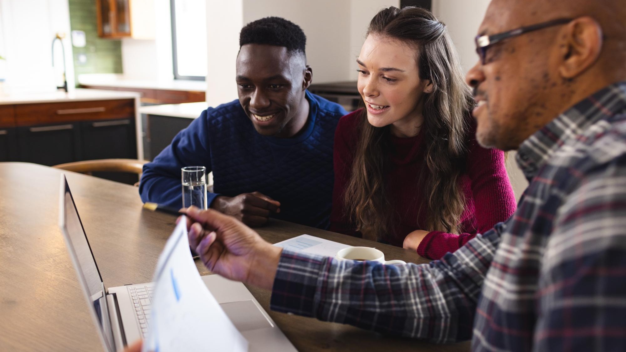 Diverse couple and biracial male financial advisor using laptop and discussing documents at home