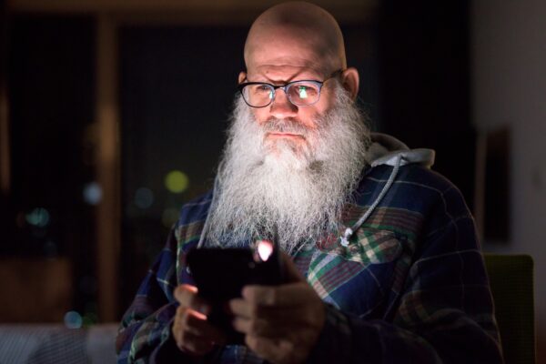 Mature bald bearded hipster man using phone at home in the dark