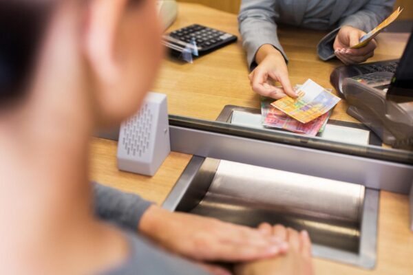 people, withdrawal, money, saving and finance concept - clerk counting swiss francs cash at bank office or currency exchanger