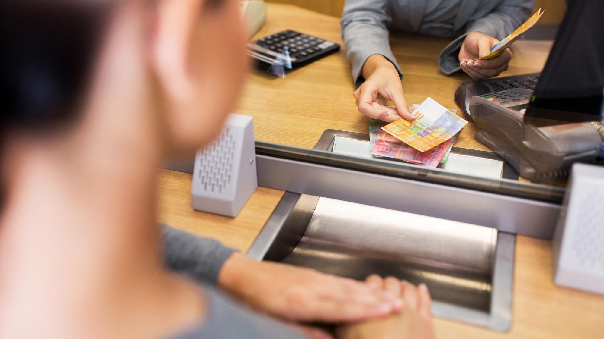 people, withdrawal, money, saving and finance concept - clerk counting swiss francs cash at bank office or currency exchanger