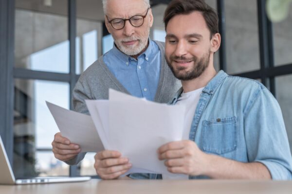 Caring loving adult son helping his old senior elderly father paying bills counting money doing paperwork at home together Aid to elderly generation Happy fathers day