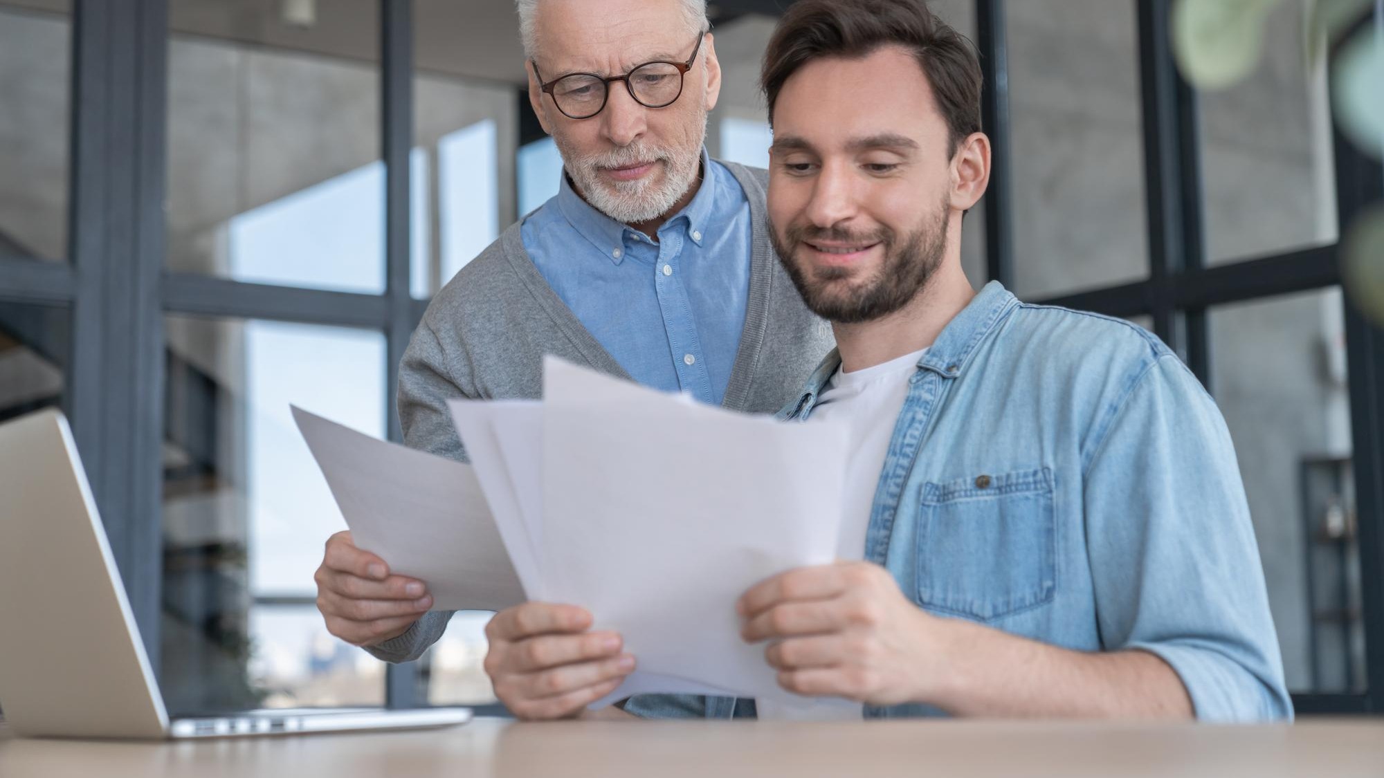 Caring loving adult son helping his old senior elderly father paying bills counting money doing paperwork at home together Aid to elderly generation Happy fathers day