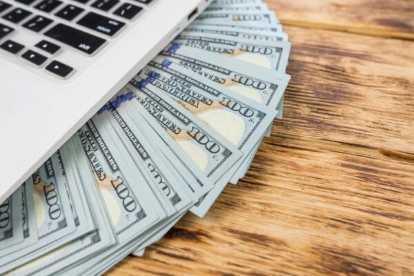 Part of a laptop and one hundred dollar American banknotes Online shopping concept