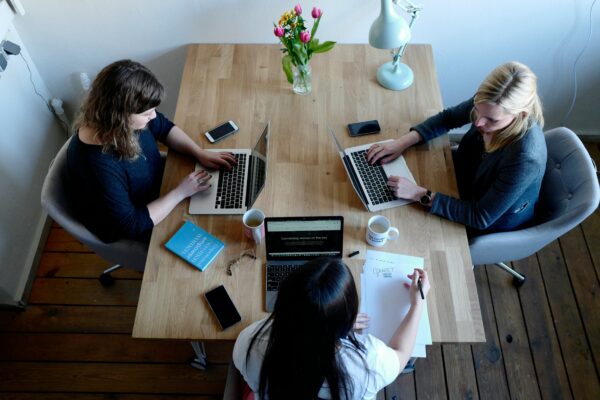 three women sitting around table using laptops