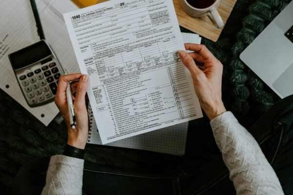 Hands holding tax forms with calculator and laptop.