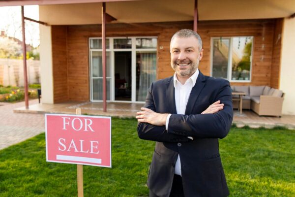 Happy middle aged european real estate agent standing outdoors in front of new house for sale