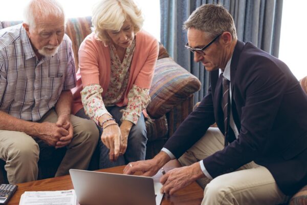 Matured male physician and senior couple discussing over laptop at retirement home