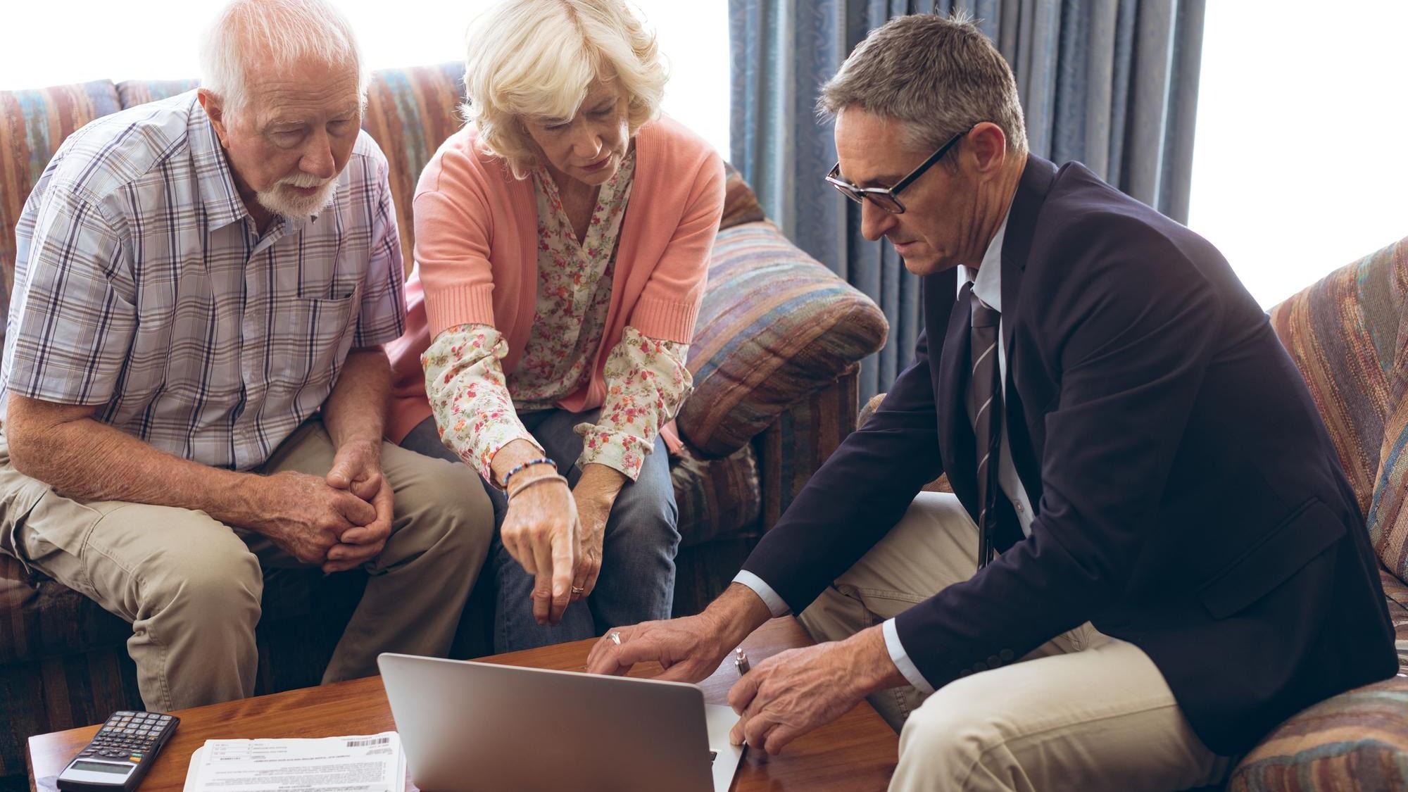 Matured male physician and senior couple discussing over laptop at retirement home