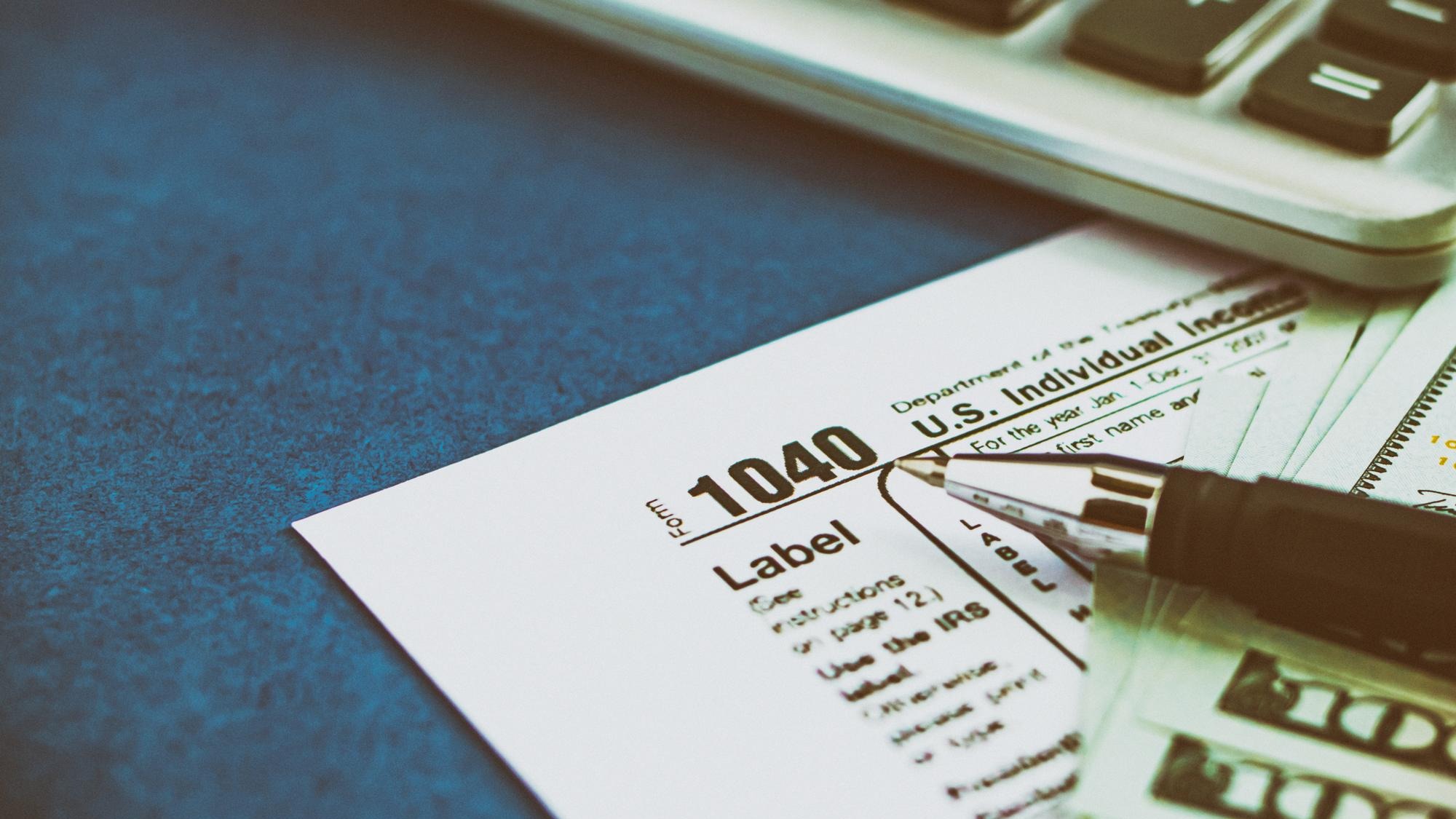 Tax form 1040 pen calculator and dollars on a blue table The concept of business taxation and business