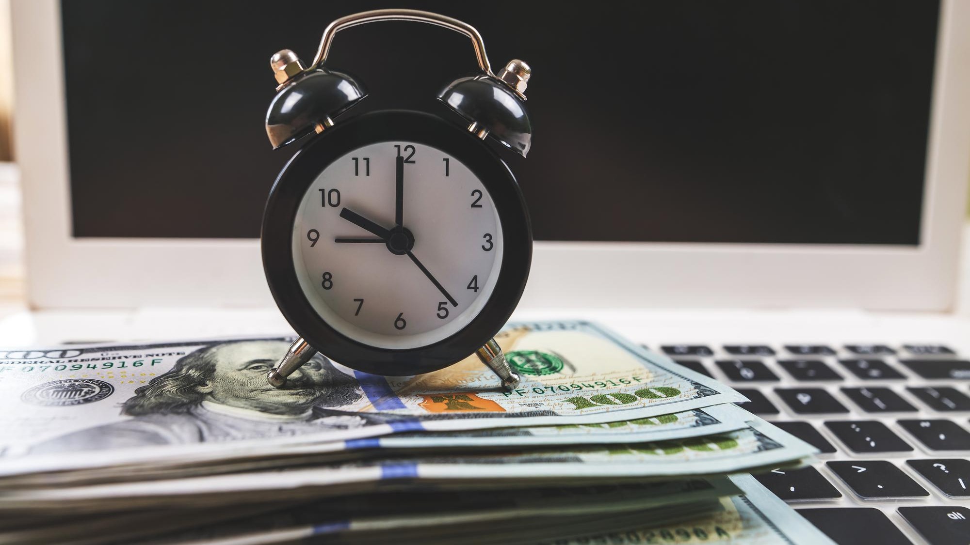 Closeup of an alarm clock with dollars on a laptop keyboard Online shopping concept