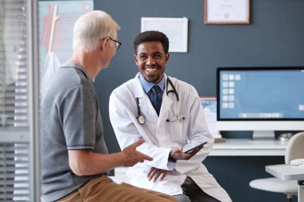 Smiling black doctor holding tablet talking to senior patient in consultation