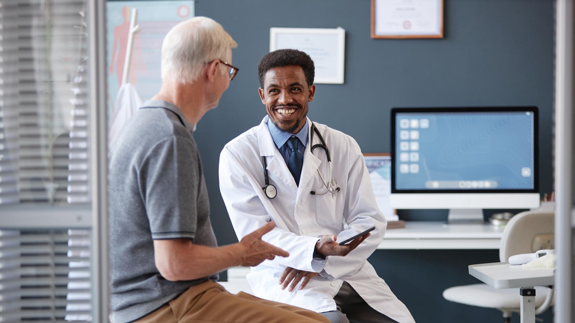 Smiling black doctor holding tablet talking to senior patient in consultation