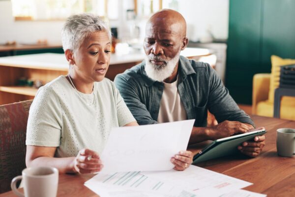 Mature interracial couple and documents with tablet for financial discussion planning or expenses at home Man woman or mortgage with paperwork or technology for payment due finance or bills