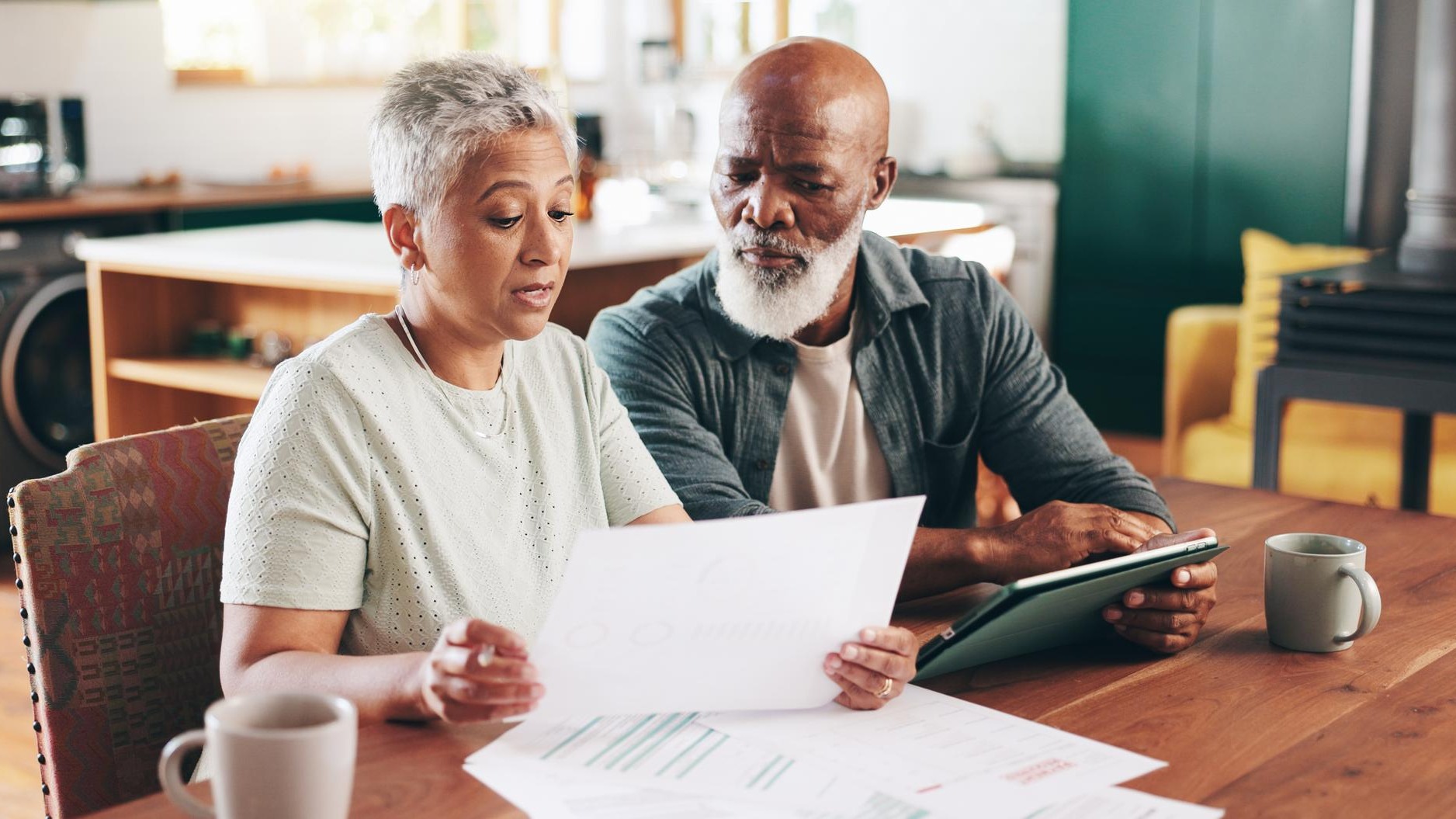 Mature interracial couple and documents with tablet for financial discussion planning or expenses at home Man woman or mortgage with paperwork or technology for payment due finance or bills
