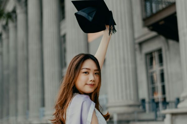 a woman in a graduation gown holding up a black hat