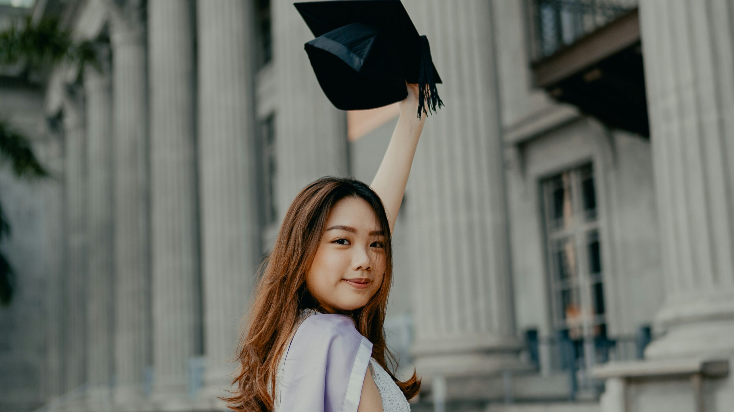 a woman in a graduation gown holding up a black hat