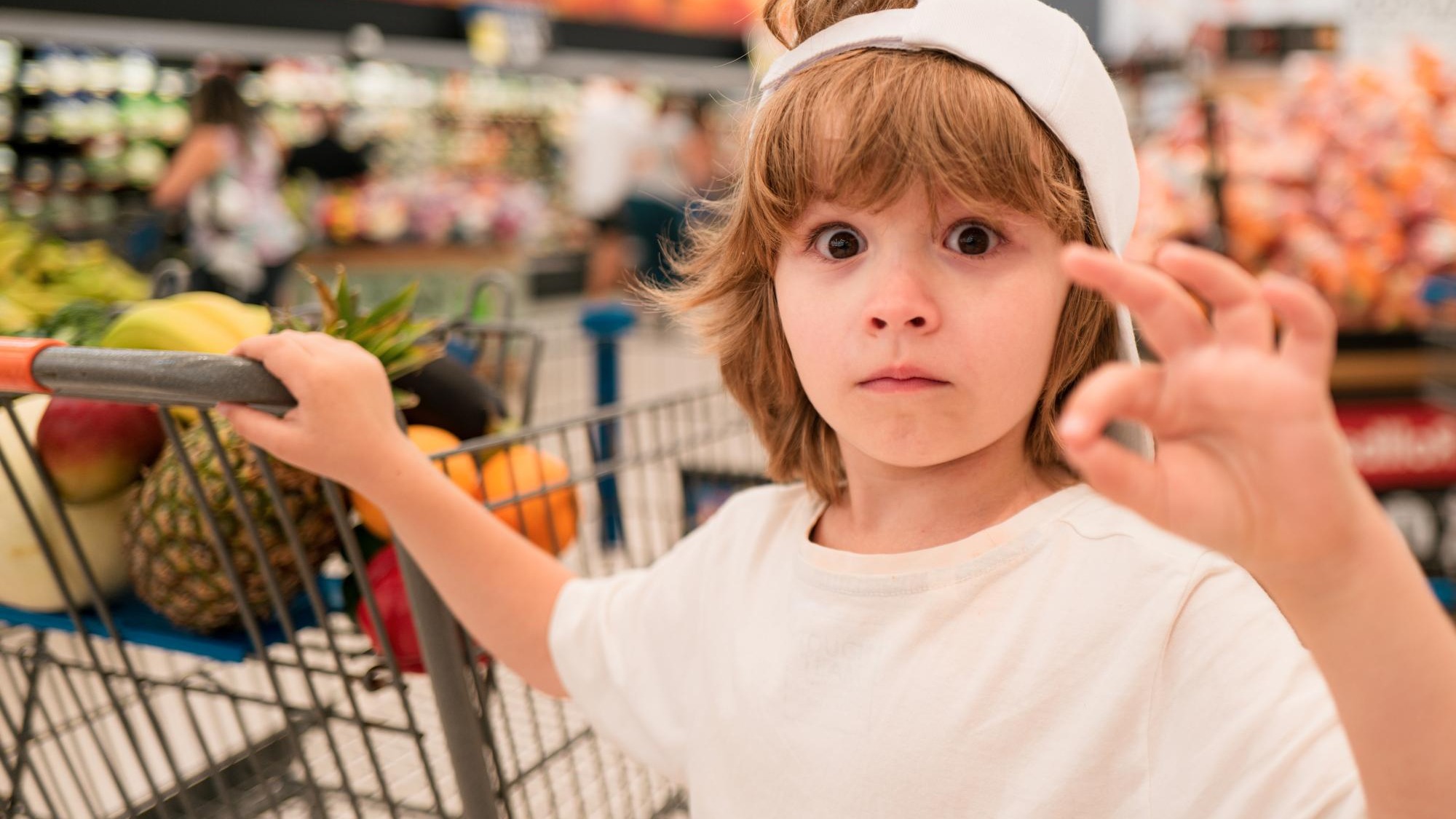 Funny little child holding shopping bag full of fresh vegetables in supermarket or store