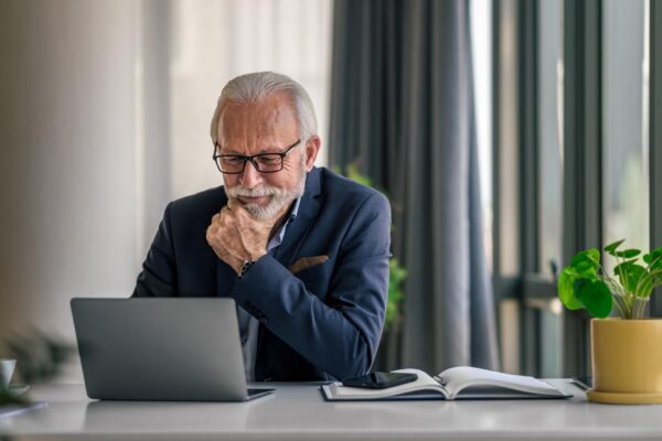 Serious elderly entrepreneur working on laptop while sitting at office desk
