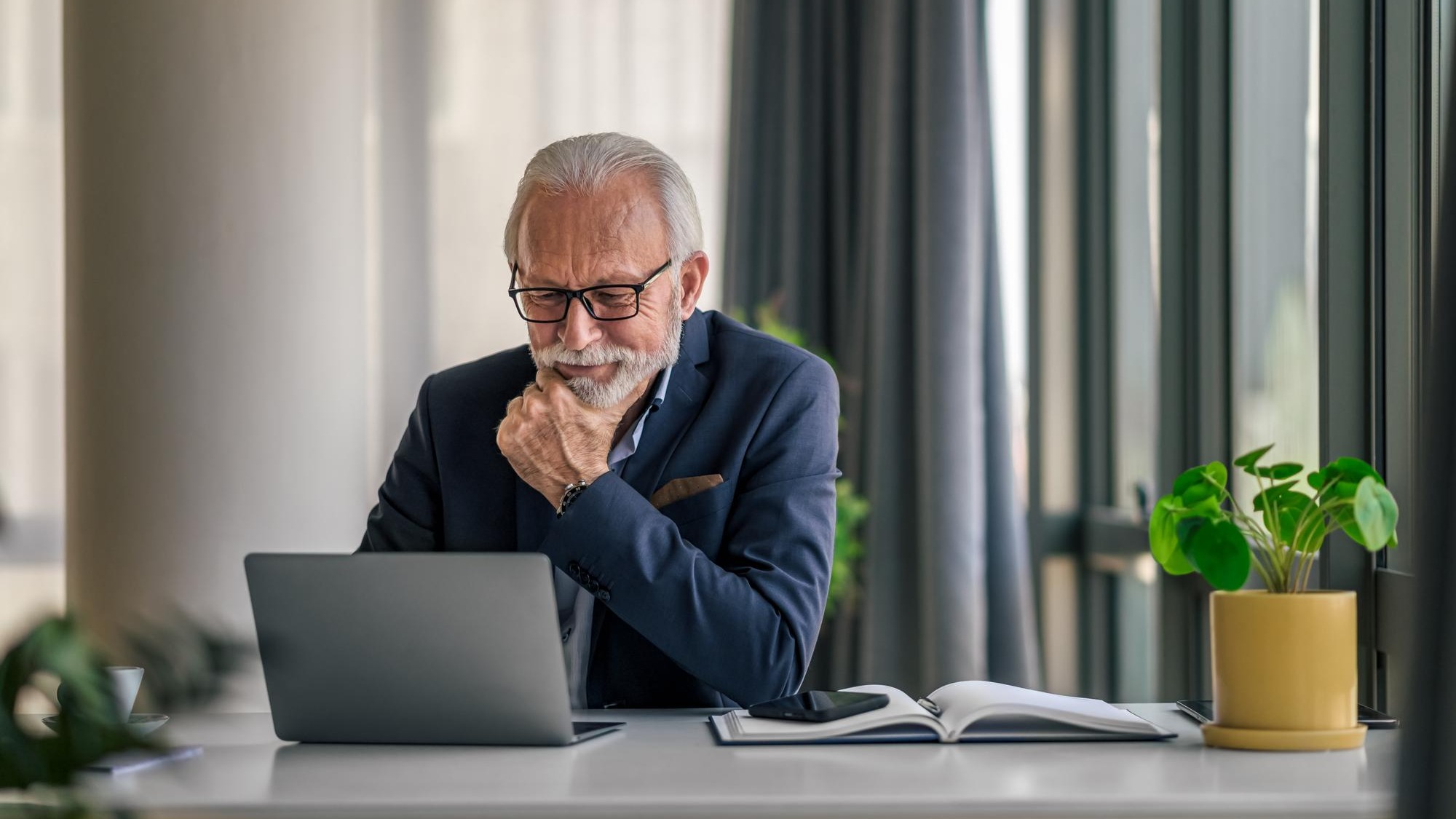 Serious elderly entrepreneur working on laptop while sitting at office desk