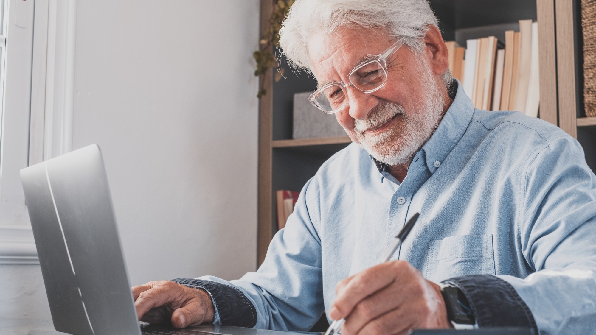 Happy old caucasian businessman smiling working online watching webinar podcast on laptop and learning education course conference calling make notes sit at work desk, elearning concept
