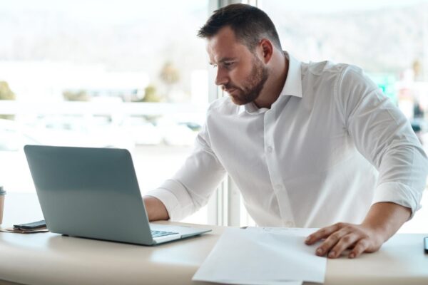Laptop documents and car sales man with invoice quote and financial report for retail or transportation industry Focus busy and professional dealership person or boss on computer with paperwork