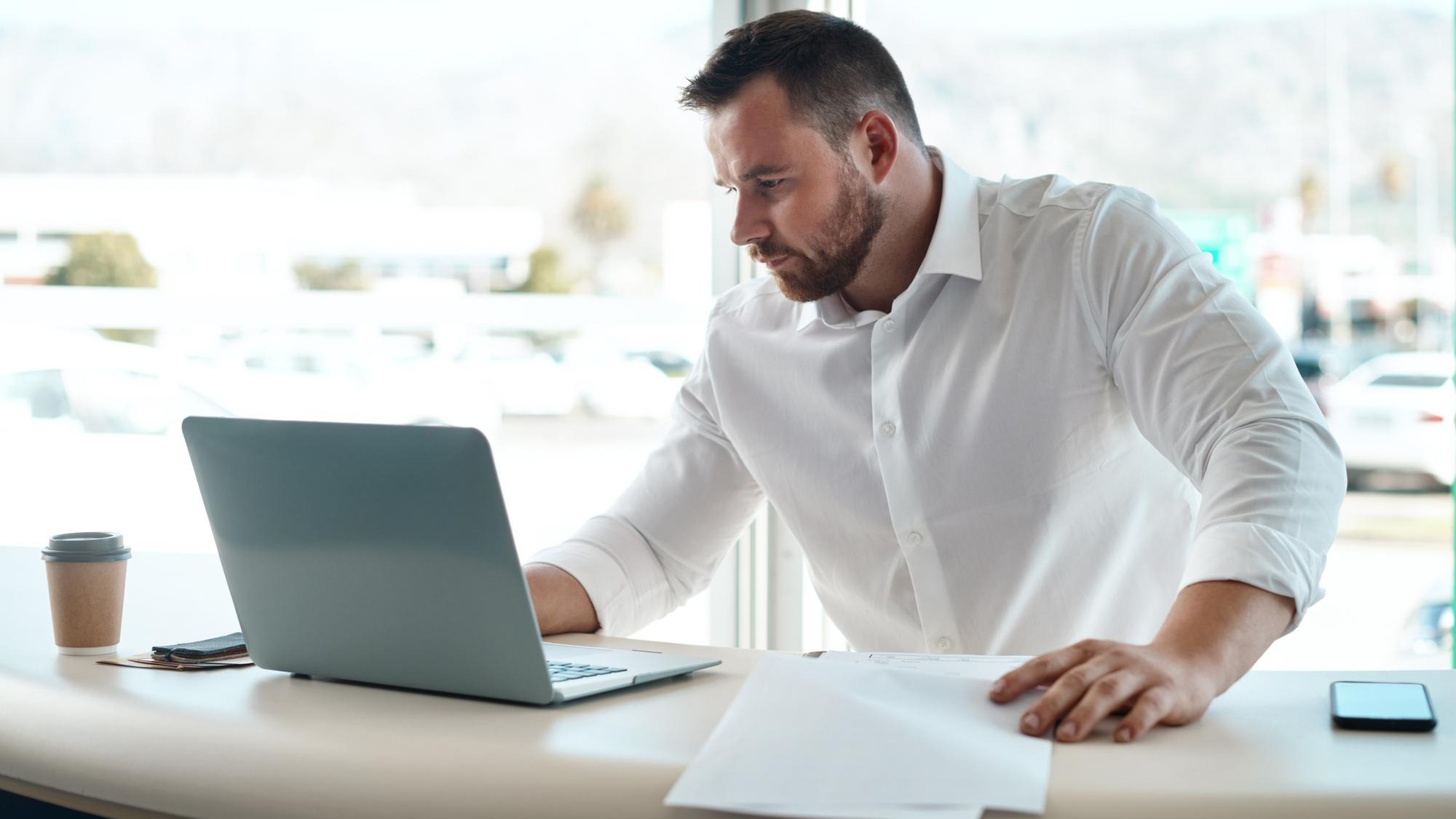 Laptop documents and car sales man with invoice quote and financial report for retail or transportation industry Focus busy and professional dealership person or boss on computer with paperwork