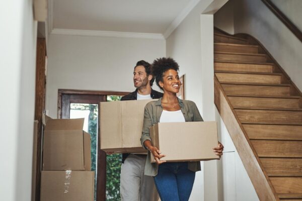 Excited happy and young couple moving into a new home together while carrying and packing household boxes Smiling positive and cheerful husband and wife in a lovely modern real estate property
